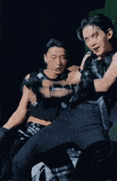 a man in a black tank top is being held by another man in a black leather outfit