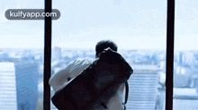 a man is standing in front of a large window holding a large bag .