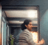 a man in a striped shirt is standing in a hallway with a plant in the background