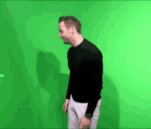 a man in a black sweater and white pants stands in front of a green screen