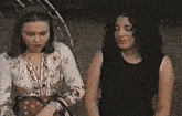 two women are standing next to each other in front of a playground in a park .