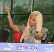 a woman is sitting at a table with her hand in the air and saying `` get it girl '' .