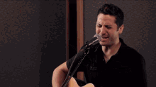 a man singing into a microphone with his eyes closed and a black shirt on