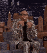 a man in a suit and glasses is sitting in a chair and making a funny face .