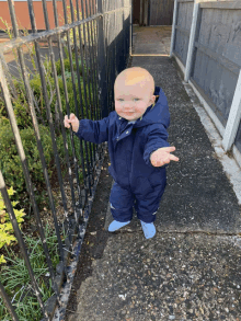 a baby is standing next to a metal fence