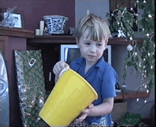 a young boy holding a yellow bucket in front of a christmas tree