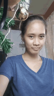a woman in a blue shirt is taking a selfie with a christmas tree in the background