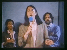 a woman is speaking into a microphone in front of a group of people on a television screen .