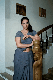 a woman in a gray saree is standing on a set of stairs