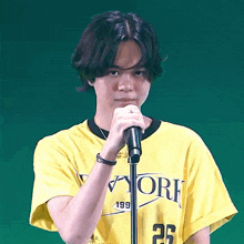 a young man wearing a yellow new york t-shirt holds a microphone