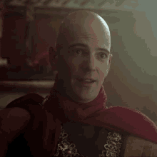 a bald man with a red scarf around his neck smiles