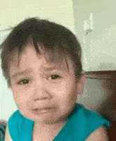 a baby in a blue shirt is crying with his eyes closed .
