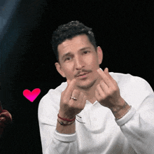 a man in a white shirt is making a heart shape with his fingers