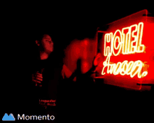 a man is standing in front of a neon sign that reads hotel amazon