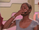 a woman is covering her mouth with her hand while wearing a gray shirt that says cw