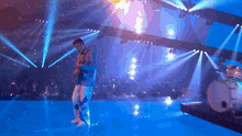 a man is playing a guitar on a stage with a drum set in the background