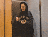 a woman in a hoodie and glasses is standing in an elevator .