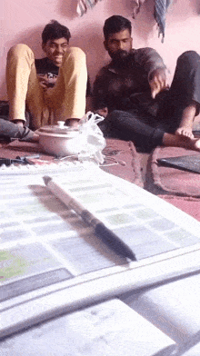 two men are sitting on the floor and one is wearing a black shirt that says ' a ' on it