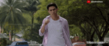 a man in a pink shirt is walking down a street in front of a sign that says ' terbaik ' on it