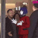 a man in a red suit and white gloves is standing next to a robot with blue hair