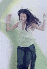 a woman wearing a white tank top and black pants is jumping in the air