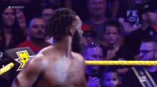 a man without a shirt is standing in a wrestling ring with a crowd behind him .