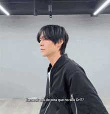 a man in a black jacket is standing in a room and talking to someone in spanish .