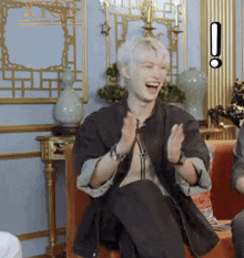 a man with white hair is sitting on a couch with his hands in the air .