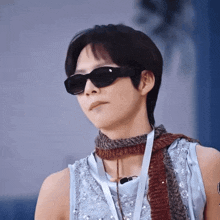 a man wearing sunglasses and a scarf looks at the camera