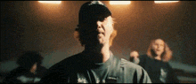 a man wearing a hat and a necklace is standing in front of a group of people in a dark room .