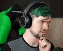 a man with green hair is wearing headphones and thinking .