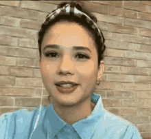 a woman wearing a headband and a blue shirt is standing in front of a brick wall and smiling .