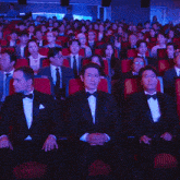 a group of people in tuxedos and bow ties are sitting in a theater applauding