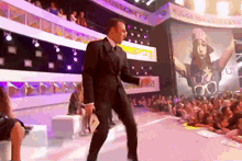 a man in a suit is dancing on a stage in front of a crowd that is watching
