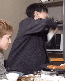 a man in a striped jacket is standing in front of a microwave while another man looks on