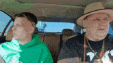 two men are sitting in a car one is wearing a hat and the other is wearing a green hoodie