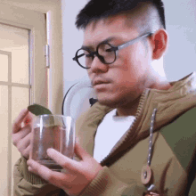 a man wearing glasses holds a glass in his hand