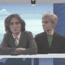 a man in a suit and a man in a green shirt are sitting next to each other