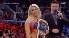 a woman is holding a wrestling championship belt while standing next to a man in a suit and tie .