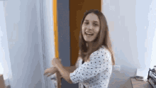 a woman in a polka dot shirt is standing in a room and opening a door .