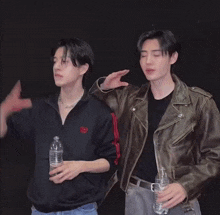 a man in a leather jacket holds a bottle of water while standing next to another man