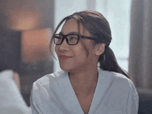 a woman wearing glasses and a white shirt looks to the side
