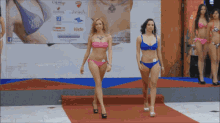 two women in bikinis walk down a red carpet in front of a sign that says viste