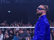a man in a blue jacket and sunglasses stands in front of a crowd wearing a shirt that says grow up