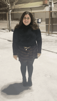 a woman wearing a black turtleneck and plaid skirt smiles in the snow