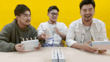 three men are sitting at a table holding boxes and one of them has a sweatshirt that says " abercrombie "
