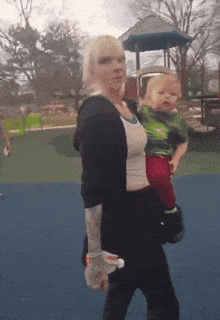 a woman is carrying a baby in a park and holding a bottle of water