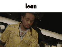 a man wearing a yellow shirt and a necklace is leaning on a table