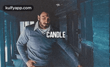 a man in a blue sweater is standing in a hallway with the word candle on his chest .