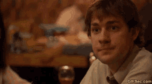 a man in a white shirt and tie is sitting at a table making a funny face .